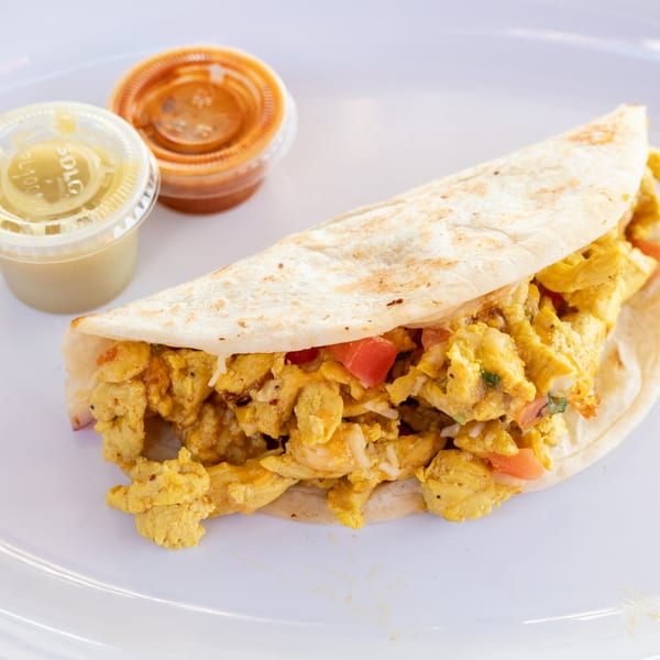 A Super Burrito breakfast taco filled with scrambled eggs, tomatoes, and rice, with two salsa cups.