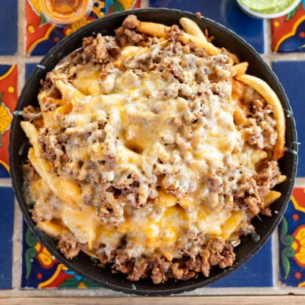 Super Burrito's carne asada fries, topped with melted cheese and ground beef, on a colorful tiled table.