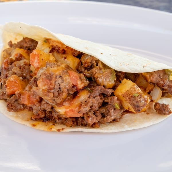A Super Burrito taco filled with seasoned ground beef, melted cheese, and diced tomatoes on a white plate.