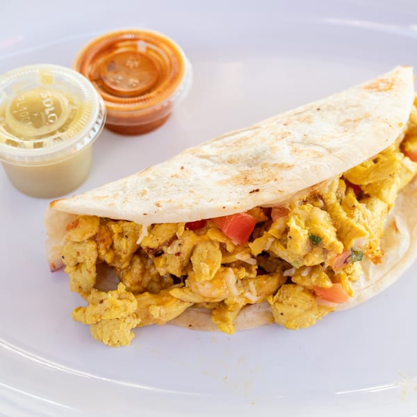 A Super Burrito breakfast burrito with scrambled eggs, tomatoes, and rice, served with two sauces.
