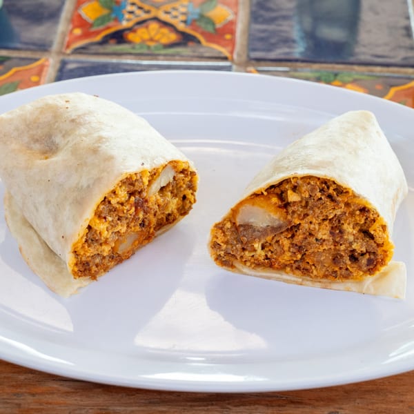 Two halves of a Super Burrito, filled with chorizo, eggs, and potatoes, on a white plate.