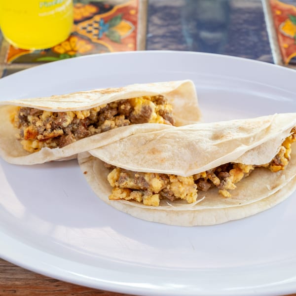 Two Super Burrito breakfast tacos with scrambled eggs and chorizo on a white plate.