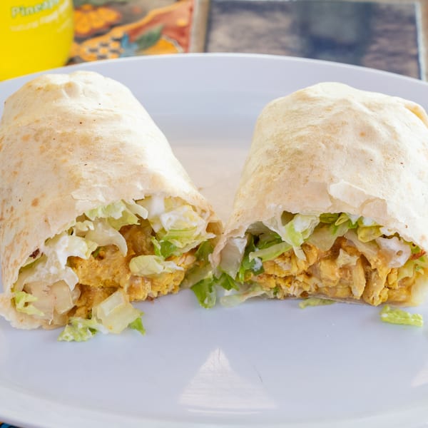 Two halves of a Super Burrito, filled with chicken, lettuce, and white sauce, on a white plate.