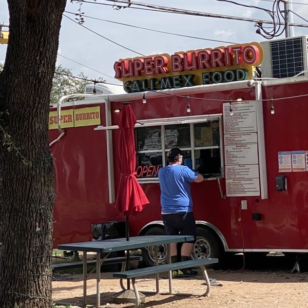 A customer orders from the red Super Burrito food truck with a picnic table in front.