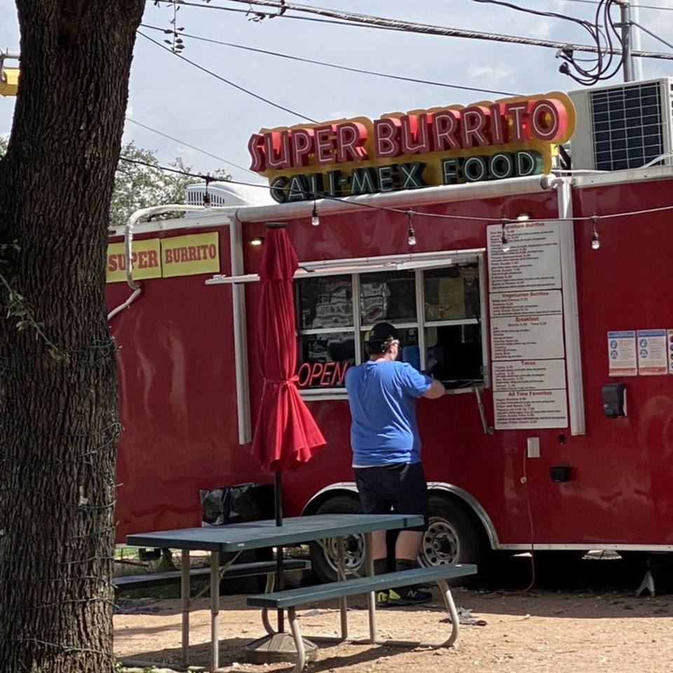 A customer orders from the red Super Burrito food truck with a picnic table in front.
