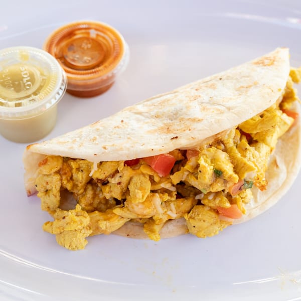 A Super Burrito breakfast taco with scrambled eggs, tomatoes, and rice, served with two sauces.