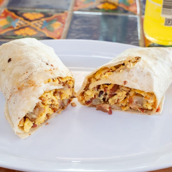 A Super Burrito breakfast burrito, cut in half, revealing scrambled eggs, potatoes, and bacon.