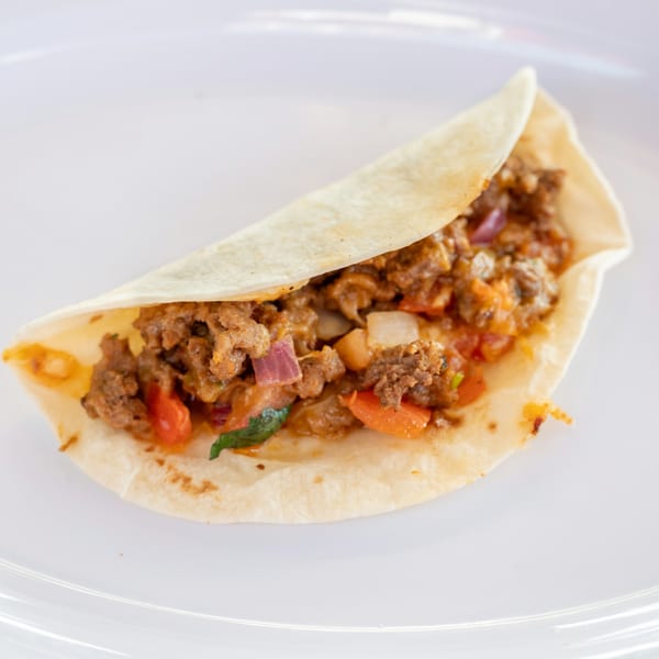 A Super Burrito taco with seasoned ground meat, red onions, and peppers on a white plate.