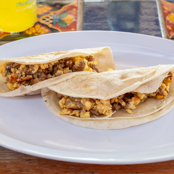 Two Super Burrito breakfast tacos filled with scrambled eggs and chorizo on a white plate.