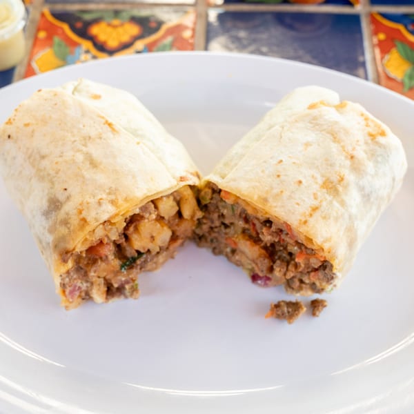 A Super Burrito, cut in half, revealing a hearty filling of meat and potatoes on a white plate.