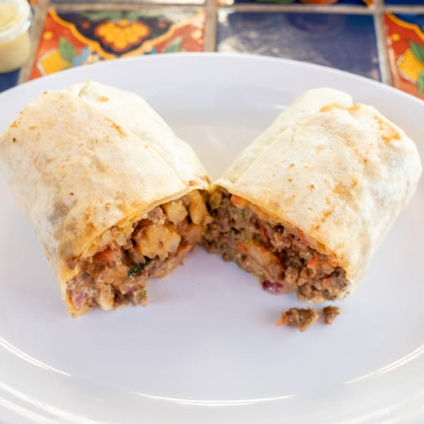 A Super Burrito, cut in half, revealing a hearty filling of meat and potatoes on a white plate.