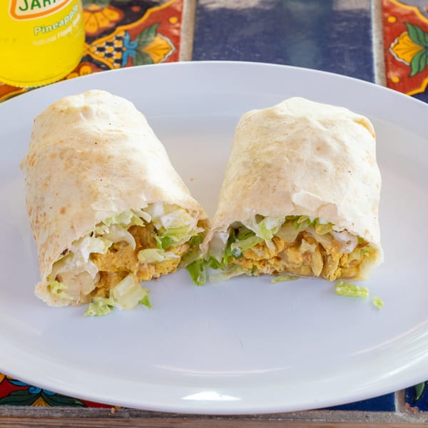 Two halves of a Super Burrito, filled with chicken and lettuce, on a white plate.