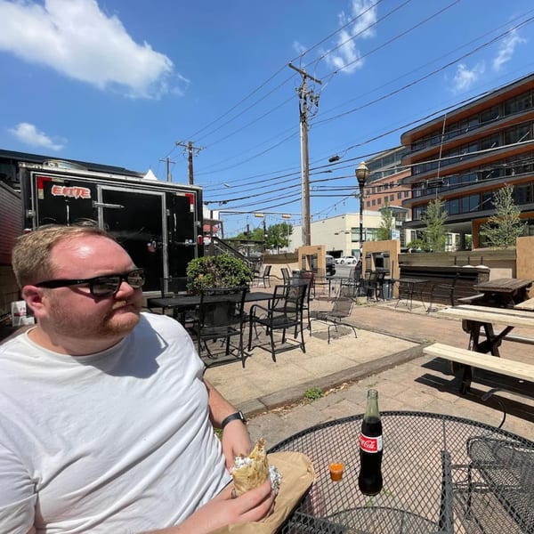 Man in sunglasses eating a Super Burrito on an outdoor patio with a Coca-Cola.