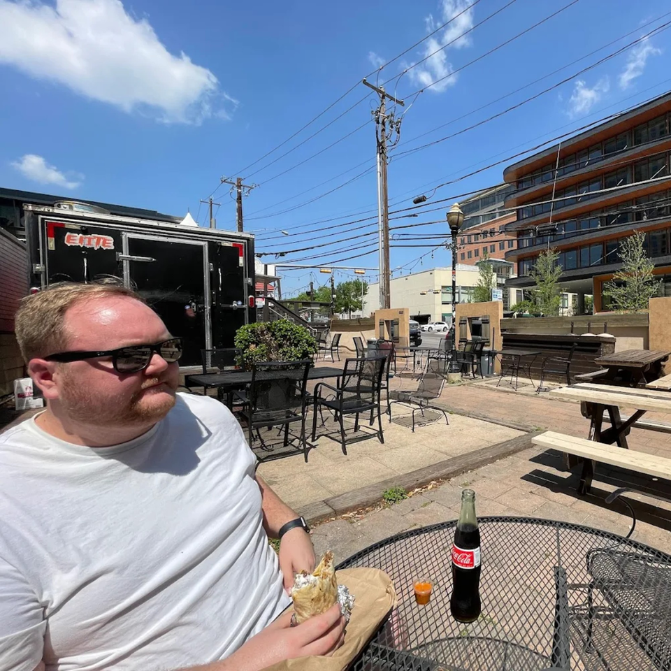 Man in sunglasses eating a Super Burrito on an outdoor patio with a Coca-Cola.
