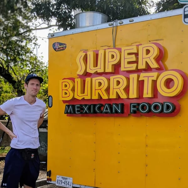 A man stands next to the yellow Super Burrito Mexican Food truck with large red and yellow lettering.