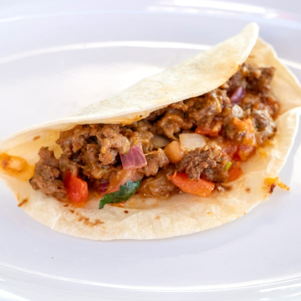 A Super Burrito taco filled with seasoned ground meat, red onions, and bell peppers on a white plate.
