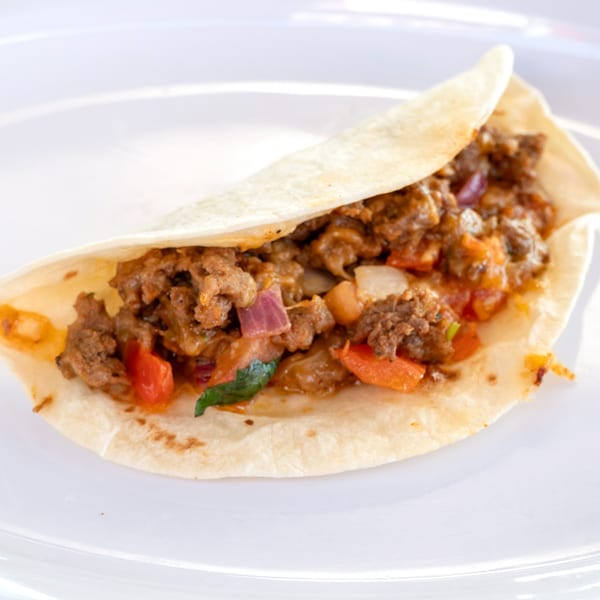 A Super Burrito taco with seasoned ground beef, red onions, and bell peppers on a white plate.