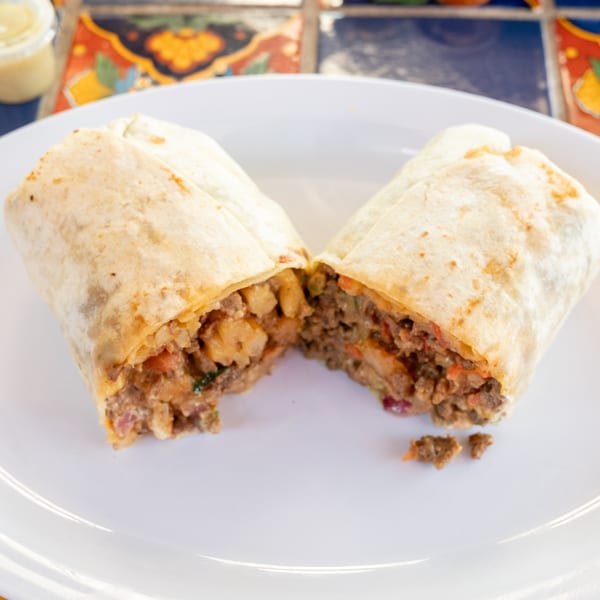 A Super Burrito, cut in half, revealing a hearty filling of meat and potatoes on a white plate.